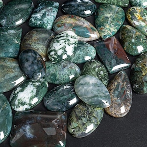 May include: A collection of green, brown, and white moss agate stones. The stones are polished and have a variety of shapes and sizes. They are arranged on a black background.