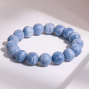 Puede incluir: Una pulsera con grandes cuentas redondas en tonos azul claro y blanco. Las cuentas tienen un aspecto veteado, creando un patrón único. La pulsera es probablemente de piedra o vidrio y es una pieza de joyería.