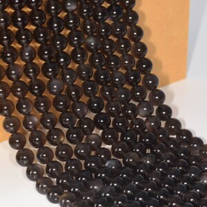 May include: A strand of black gemstone beads, each bead is round and smooth. The beads are strung together on a clear thread.