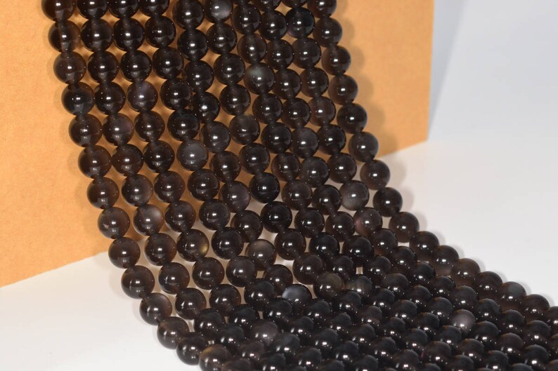 May include: A strand of black gemstone beads, each bead is round and smooth. The beads are strung together on a clear thread.