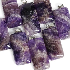 May include: A collection of rectangular amethyst pendants, each featuring a polished surface with natural purple and white mineral inclusions. Every pendant is fitted with a silver-toned metal bail at the top for attachment to a necklace chain.