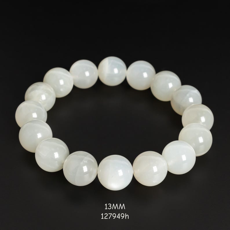 May include: A white beaded bracelet with 13mm beads. The bracelet is made of round, polished beads, strung together to form a circular shape. The text "13MM 127949h" is at the bottom of the image.