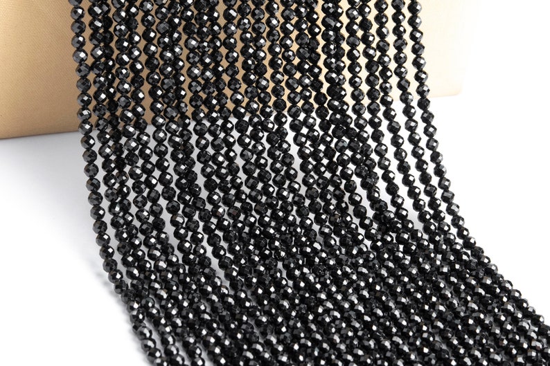 May include: A strand of black faceted beads, likely made of black spinel or black diamond, for jewelry making.