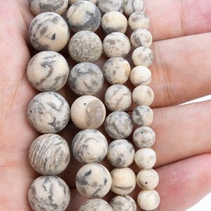 May include: A strand of white and gray agate beads with a marbled pattern. The beads are round and smooth, and they are arranged in a graduated size order, with the largest beads at the top and the smallest beads at the bottom.