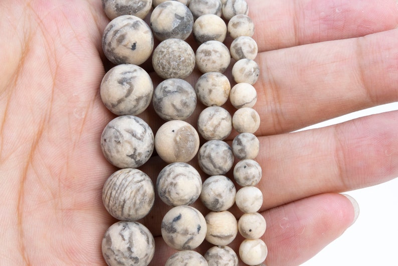 May include: A strand of white and gray agate beads with a marbled pattern. The beads are round and smooth, and they are arranged in a graduated size order, with the largest beads at the top and the smallest beads at the bottom.