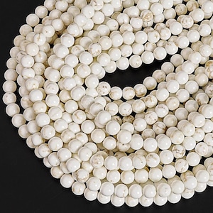 May include: A close-up shot of a collection of white round beads with subtle brown marbling. The beads are strung together, creating a spiral pattern. The beads are smooth and have a matte finish. The beads are likely used for jewelry making.