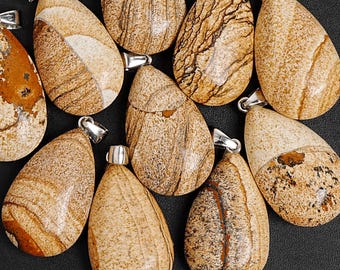 Puede incluir: Una colección de colgantes en forma de lágrima de piedra arenisca con enganches plateados. Los colgantes presentan una mezcla de tonos beige, marrón y crema con patrones naturales únicos. Ideales para la creación de joyas.