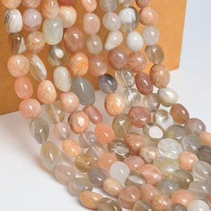 May include: A strand of sunstone beads in various shades of peach, white, and gray. The beads are smooth and oval-shaped, with a natural, polished finish.