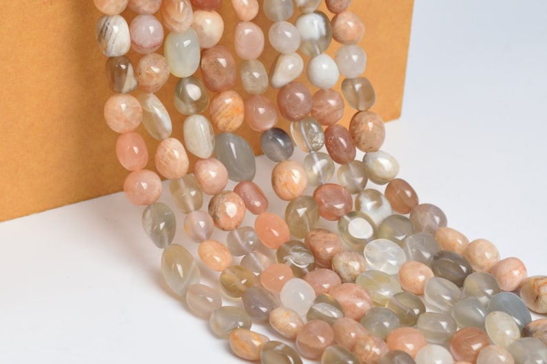 May include: A strand of sunstone beads in various shades of peach, white, and gray. The beads are smooth and oval-shaped, with a natural, polished finish.