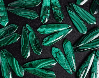 May include: A collection of green malachite gemstone pendants with a variety of shapes and patterns. The pendants are arranged on a black background.