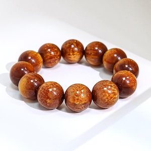 May include: A circular bracelet composed of twelve polished, spherical beads. Each bead features a warm, golden-brown hue with a distinct, swirling wood grain pattern that creates a reflective, glossy finish across the entire surface.
