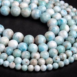 May include: A strand of light blue and white gemstone beads. The beads are round and have a smooth, polished finish. The beads are arranged in a circle, with the largest beads in the centre and the smallest beads on the outside.