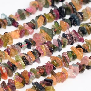 May include: Strands of raw, colorful tourmaline gemstone chips. The chips are a mix of pink, green, orange, and black, strung together. The gemstones are irregularly shaped and have a natural, rough texture.