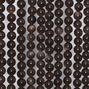 May include: A strand of dark brown gemstone beads with a subtle iridescent shimmer. The beads are round and smooth, and they are strung on a clear thread.