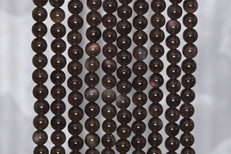 May include: A strand of dark brown gemstone beads with a subtle iridescent shimmer. The beads are round and smooth, and they are strung on a clear thread.