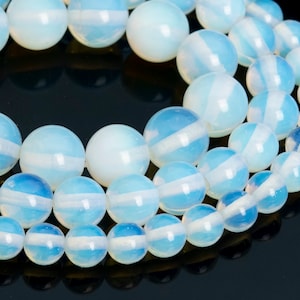May include: A strand of white opal beads with a blue iridescent sheen. The beads are round and smooth, and they are arranged in a circular pattern.