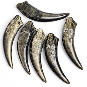 May include: Six curved pendants carved from black and gold obsidian, each featuring a detailed wolf head design at the top. The smooth, polished stone pieces have a tapered, tooth-like shape with a small hole near the top for hanging as jewelry.