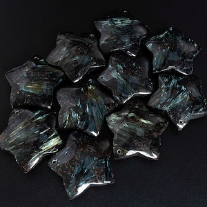May include: A group of ten star-shaped, dark blue and green gemstone pendants. The stones have a shimmery, iridescent quality.