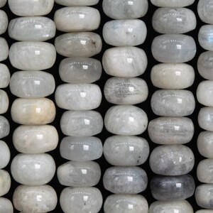May include: Rows of polished, oval-shaped moonstone beads. The beads are primarily white with subtle gray and translucent areas, creating a soft, luminous appearance. The beads are strung together, ready for jewelry making.