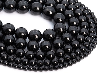 May include: A collection of glossy, black beads of varying sizes, arranged in a curved pattern against a white background. The beads have a smooth, reflective surface, suggesting they are polished. The arrangement showcases the beads' spherical shape.