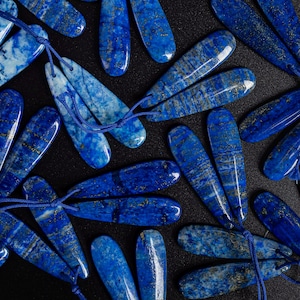 May include: A collection of blue and gold lapis lazuli gemstone teardrop pendants with string ties.