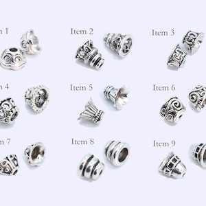 May include: Nine different silver-toned metal bead caps with various designs. The bead caps are arranged in three rows of three.