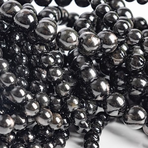 May include: A close-up of a strand of black obsidian beads. The beads are round and smooth, with a high polish. The beads are strung together on a clear thread.