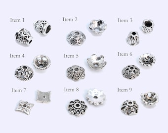 May include: Nine different silver-toned metal bead caps with various ornate designs. The bead caps are arranged in three rows of three.