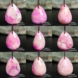May include: Nine teardrop-shaped pink stone pendants on dark cords. Each pendant features unique white and magenta marbling. Labels include codes and dimensions: 900049 28x22x6mm, 900050 24x21x9mm, 900053 29x19x8mm, 900054 27x20x8mm, 900057 31x19x9mm, 900059 29x23x8mm, 900060 32x23x7mm, 900061 27x20x11mm, and 900064 29x23x12mm.