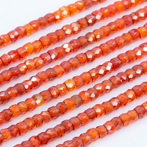 May include: A strand of orange carnelian beads, each bead is faceted and has a square shape.