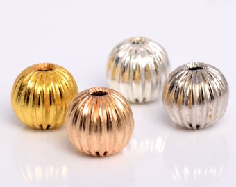Puede incluir: Cuatro cuentas redondas de metal en dorado, oro rosa y plata. Las cuentas tienen una superficie texturizada y nervada.