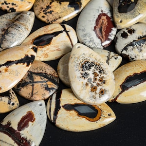 May include: A collection of teardrop-shaped, polished, natural stone pendants with a variety of brown, black, and white patterns. The stones have a smooth, glossy finish.