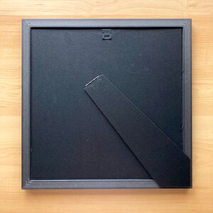 May include: The back of a black picture frame with a black easel stand.