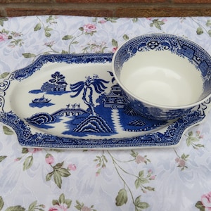 Puede incluir: Un plato de servir de porcelana azul y blanco con un tazón a juego. El plato presenta un diseño tradicional de paisaje chino con un puente, árboles y una pagoda. El tazón está vacío y listo para ser llenado.
