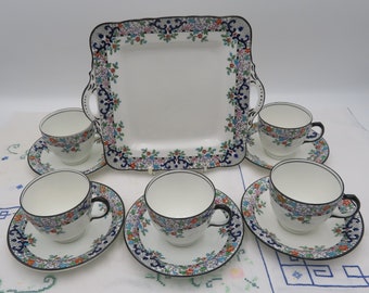 Könnte beinhalten: Ein Set aus sechs Vintage-Teetassen und Untertassen mit floralem Design. Die Tassen und Untertassen sind weiß mit schwarzem Rand und einem bunten Blumenmuster. Das Set enthält ein quadratisches Serviertablett mit passendem Blumendesign.