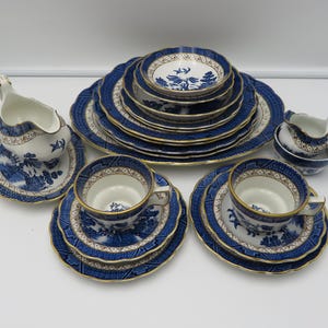 Puede incluir: Un juego de té de porcelana azul y blanco con un patrón decorativo. El juego incluye tazas, platillos, platos, cuencos y jarras de servir. Los bordes de los platos y tazas están adornados con oro.