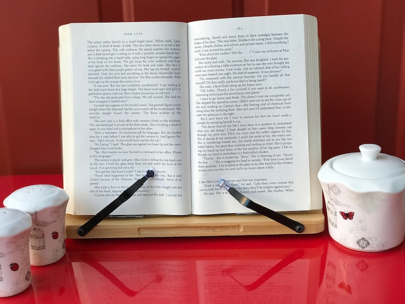 May include: A wooden book stand with two black metal page holders holding open a book with the title "Lark Love".  Two small white salt and pepper shakers with a butterfly design are on the left side of the stand. A small white sugar bowl with a butterfly design is on the right side of the stand.