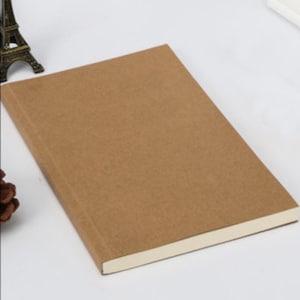 May include: A brown notebook with a cream-colored spine. The notebook is closed and lying flat on a white surface.