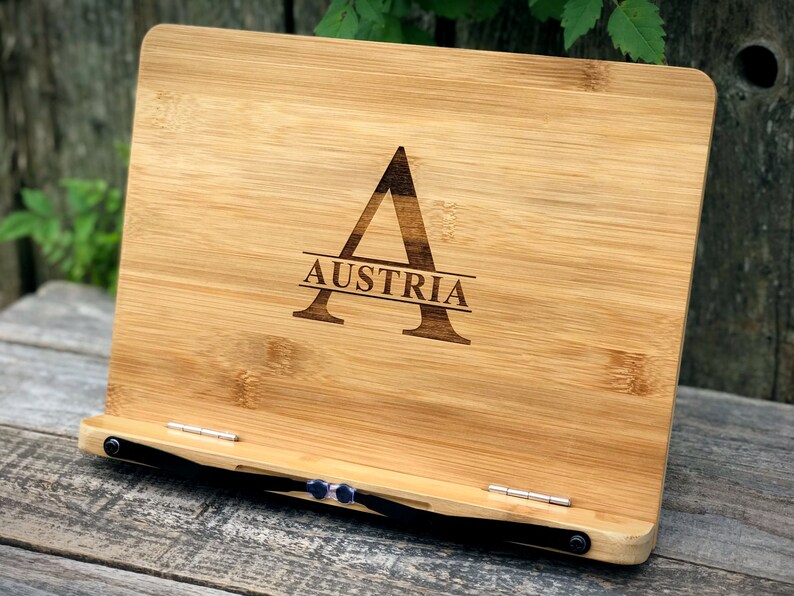 May include: A bamboo book stand with a black strap and metal hinges. The stand is engraved with the letter "A" and the word "AUSTRIA".