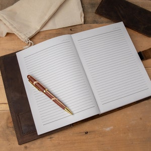 May include: A brown leather-bound journal with lined pages, a pen, and a small cloth bag. The journal is open to a blank page.
