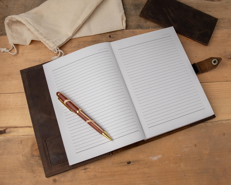 May include: A brown leather-bound journal with lined pages, a pen, and a small cloth bag. The journal is open to a blank page.