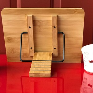 May include: A wooden book stand with a black metal frame. The stand has a tiered design and is made of natural bamboo. The stand is on a red surface.