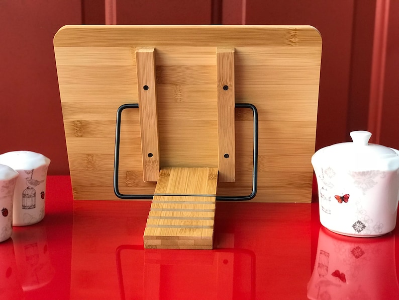May include: A wooden book stand with a black metal frame. The stand has a tiered design and is made of natural bamboo. The stand is on a red surface.
