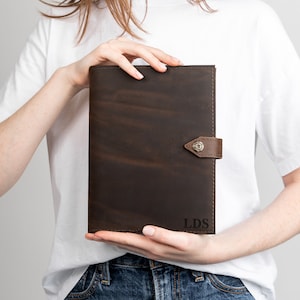 May include: A brown leather portfolio with a flap closure and a metal button. The portfolio has the initials "LDS" embossed on the front.