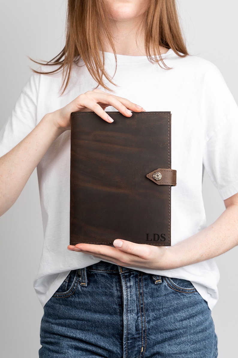 May include: A brown leather portfolio with a flap closure and a metal button. The portfolio has the initials "LDS" embossed on the front.
