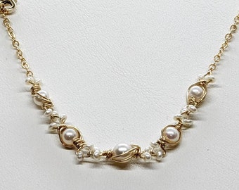 May include: A delicate gold-toned necklace featuring a series of white pearls. The necklace has a Y-shaped design with a strand of pearls hanging down. The main part of the necklace has larger pearls wrapped in gold wire, interspersed with smaller pearls.