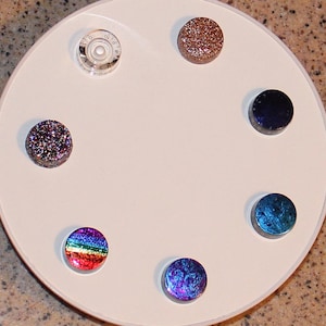 Peut inclure: Une assiette circulaire blanche avec six carreaux de verre ronds. Les carreaux sont de différentes couleurs, notamment bleu, violet, vert, rouge, marron et noir. Les carreaux ont une finition scintillante ou irisée.