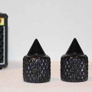 May include: Two black guitar amplifier knobs with a textured diamond pattern and a conical top. The knobs are in front of two miniature black and gold amplifiers with the word "Marshall" in white.