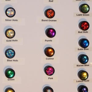 May include: A display of 16 different colored glass cabochons, each with a unique finish, including blue, red, silver holo, burnt orange, gold holo, purple, copper, blue holo, red holo, satin blue, marine blue, green, pink, lemon gold, bright gold, rainbow, and indigo.
