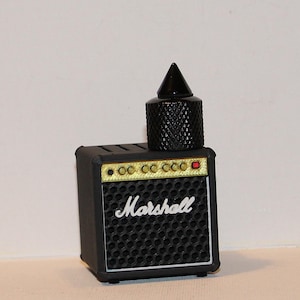 May include: A miniature black Marshall amplifier with gold trim and the brand name in white script. A black, textured, conical object sits atop the amplifier. The amplifier has a speaker grill design.